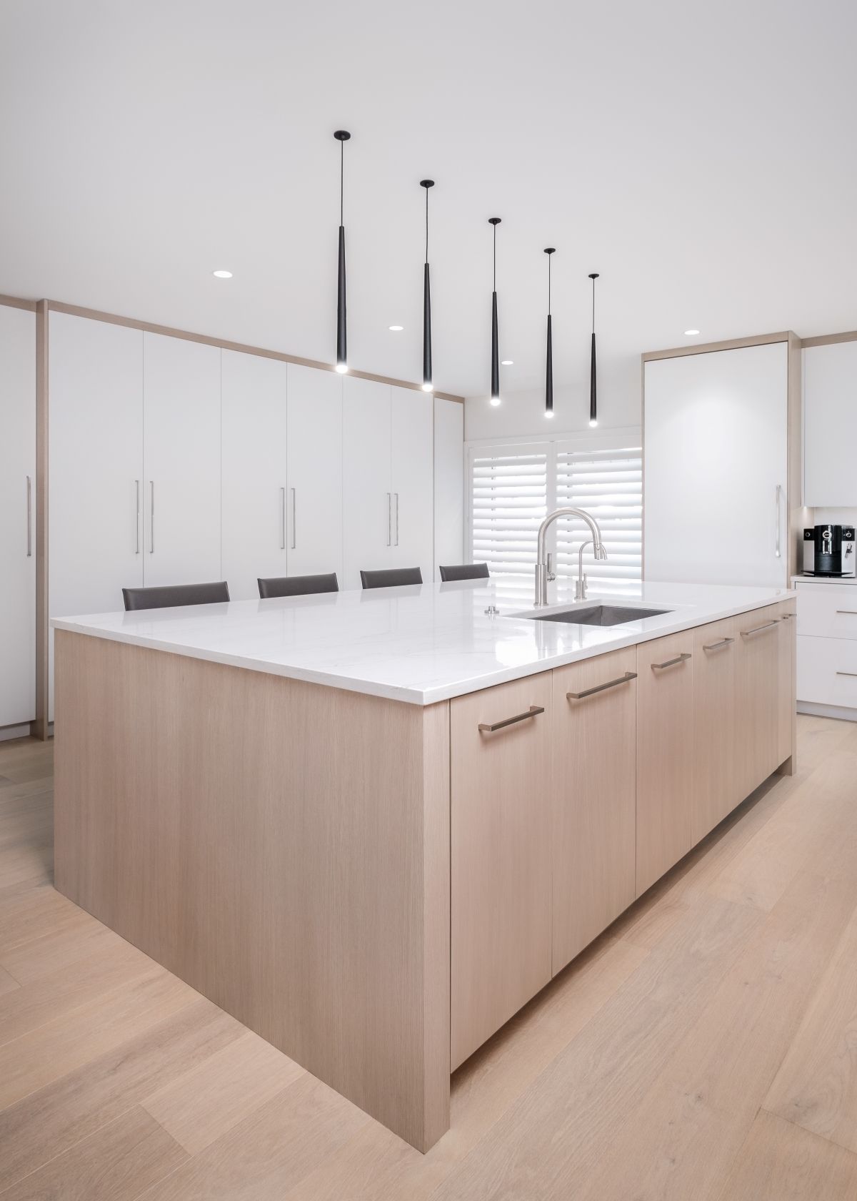 Modern white kitchen island with light wood cabinets and hanging pendant lights