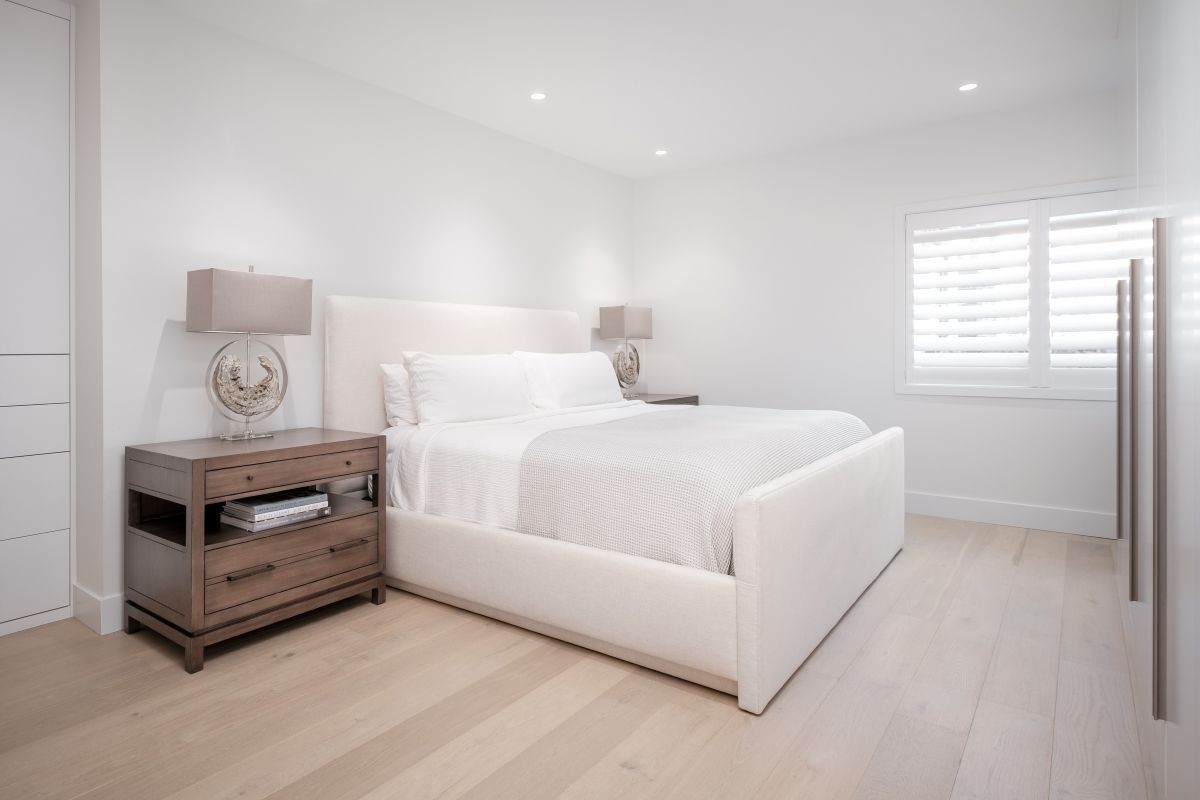 Bright minimalist bedroom with white bed, wicker nightstand, and window blinds