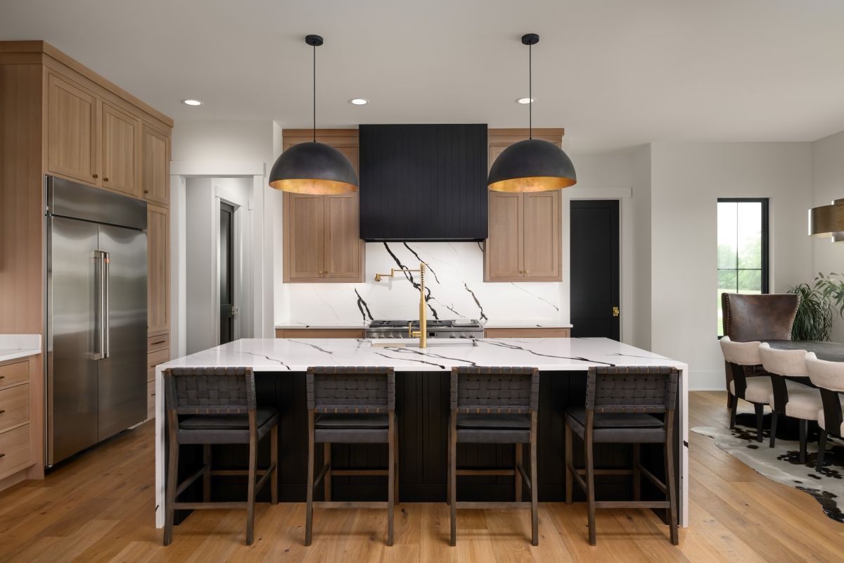 Modern kitchen with island, four stools, black pendant lights, wood cabinets, and stainless-steel appliances