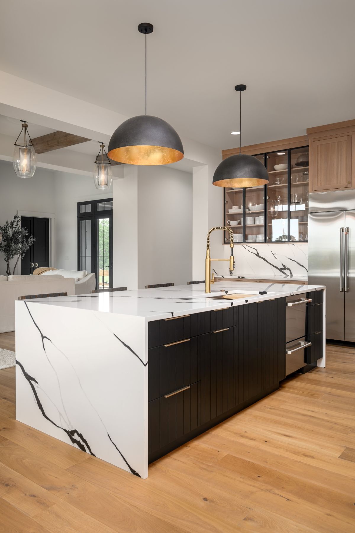 Modern kitchen with marble island, black cabinets, wood floors, and pendant lights