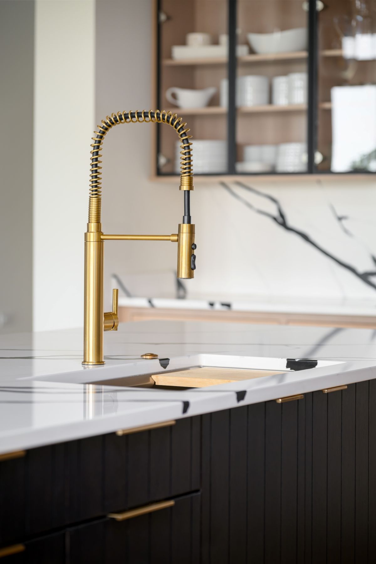 Modern kitchen sink with gold spring faucet, white countertop, and dark lower cabinets.