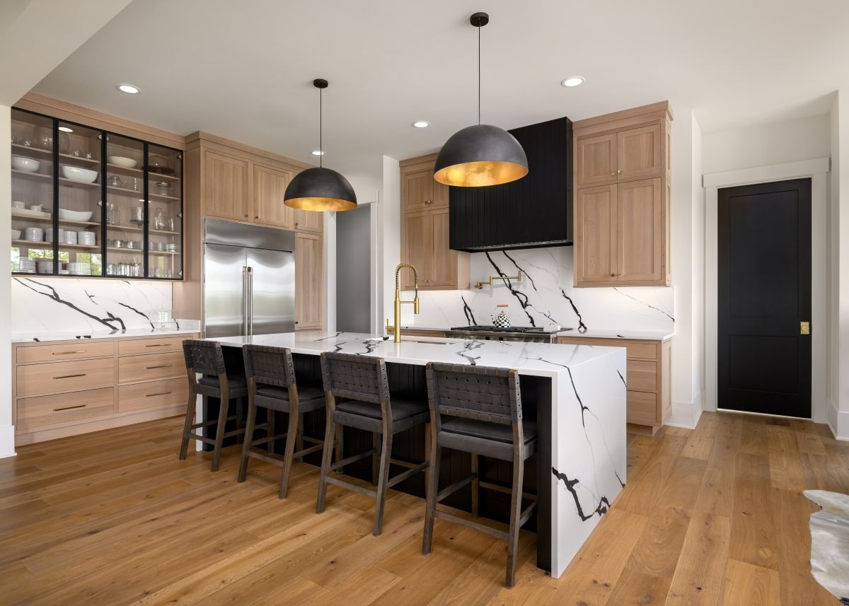 Modern kitchen with marble island, black pendant lights, wood cabinets, and hardwood floors