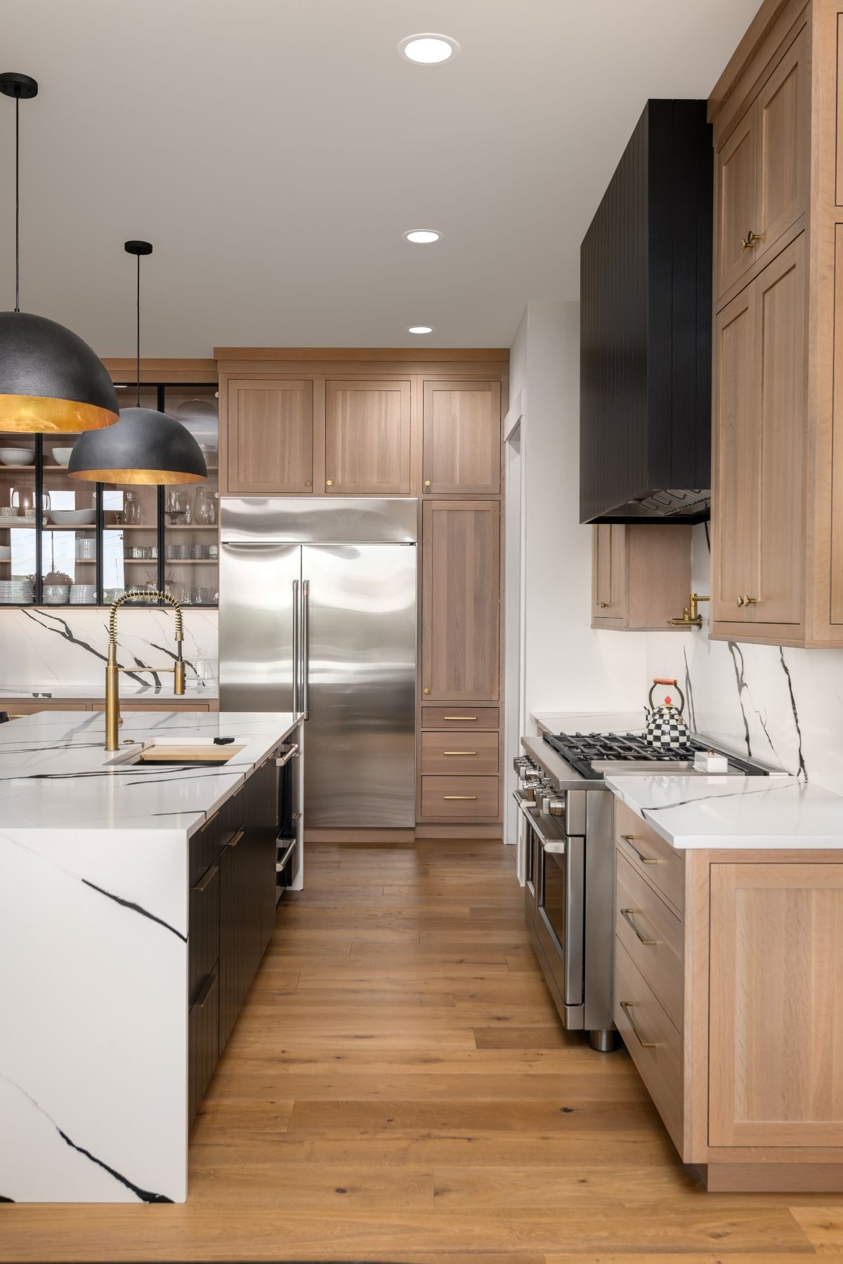 Modern kitchen with light wood cabinets, stainless steel fridge, white island, and black pendant lights