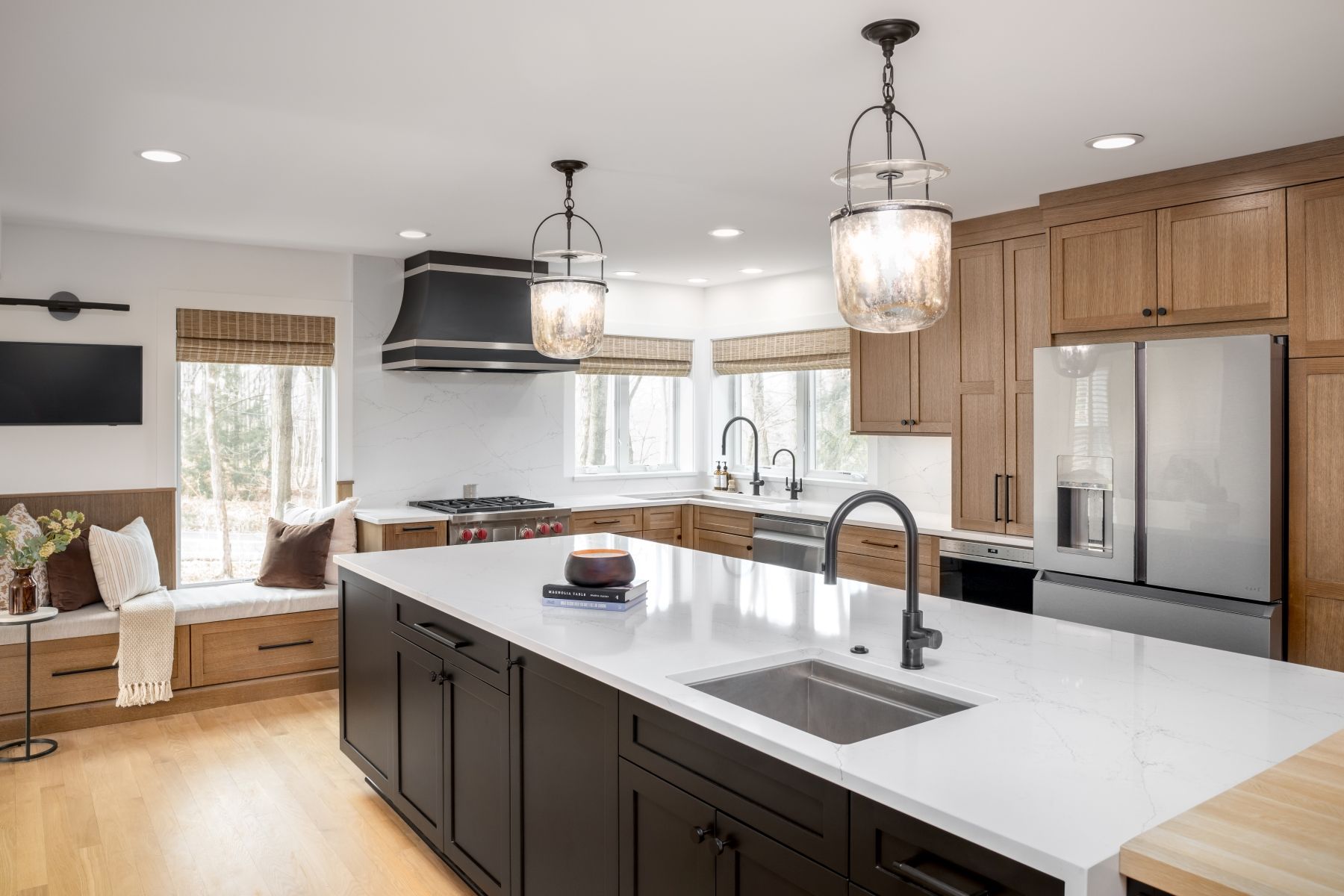 Modern kitchen with white island, dark cabinets, stainless appliances, and pendant lights