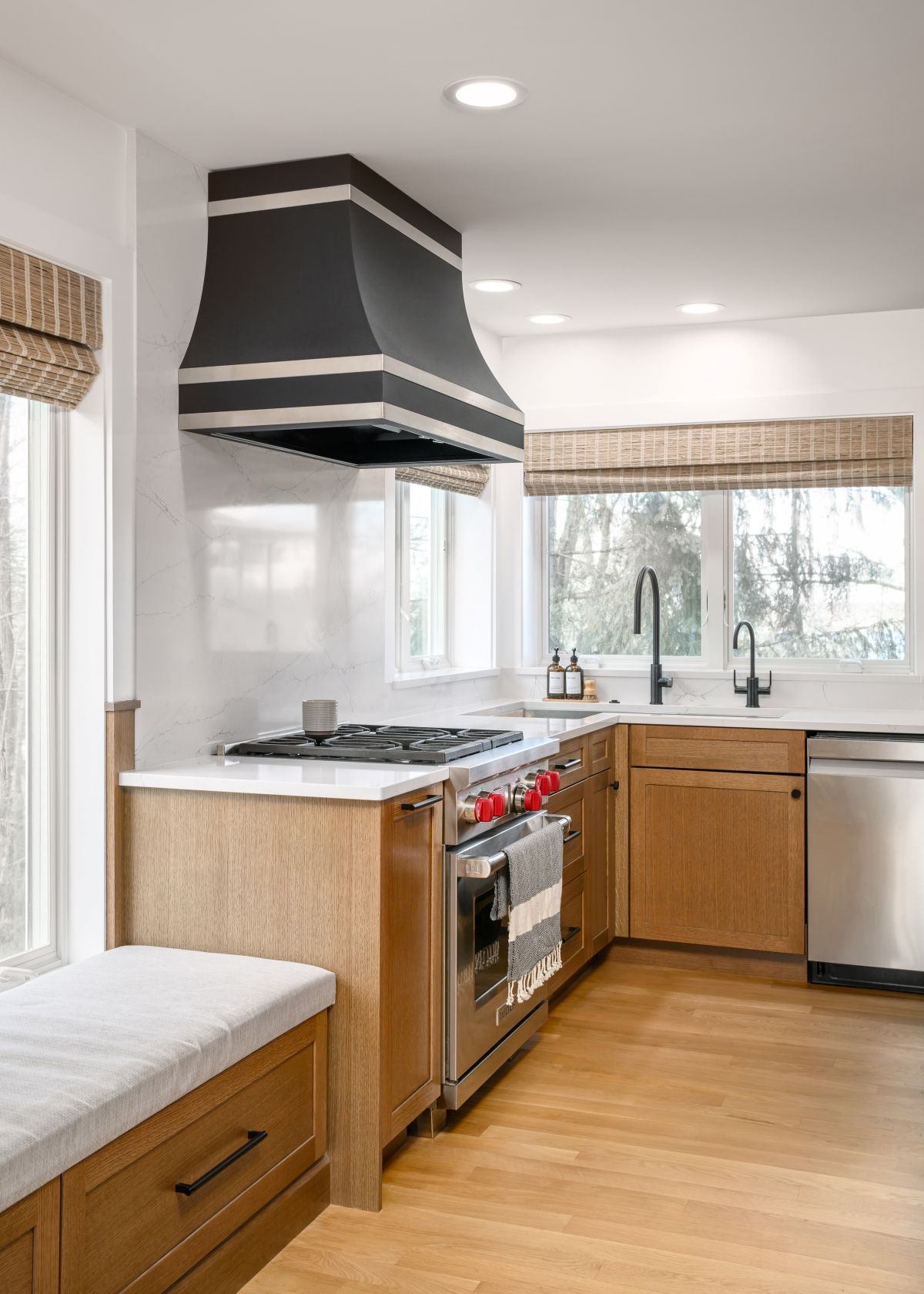 Bright kitchen with wood cabinets, stainless stove, black range hood, and a window over the sink.