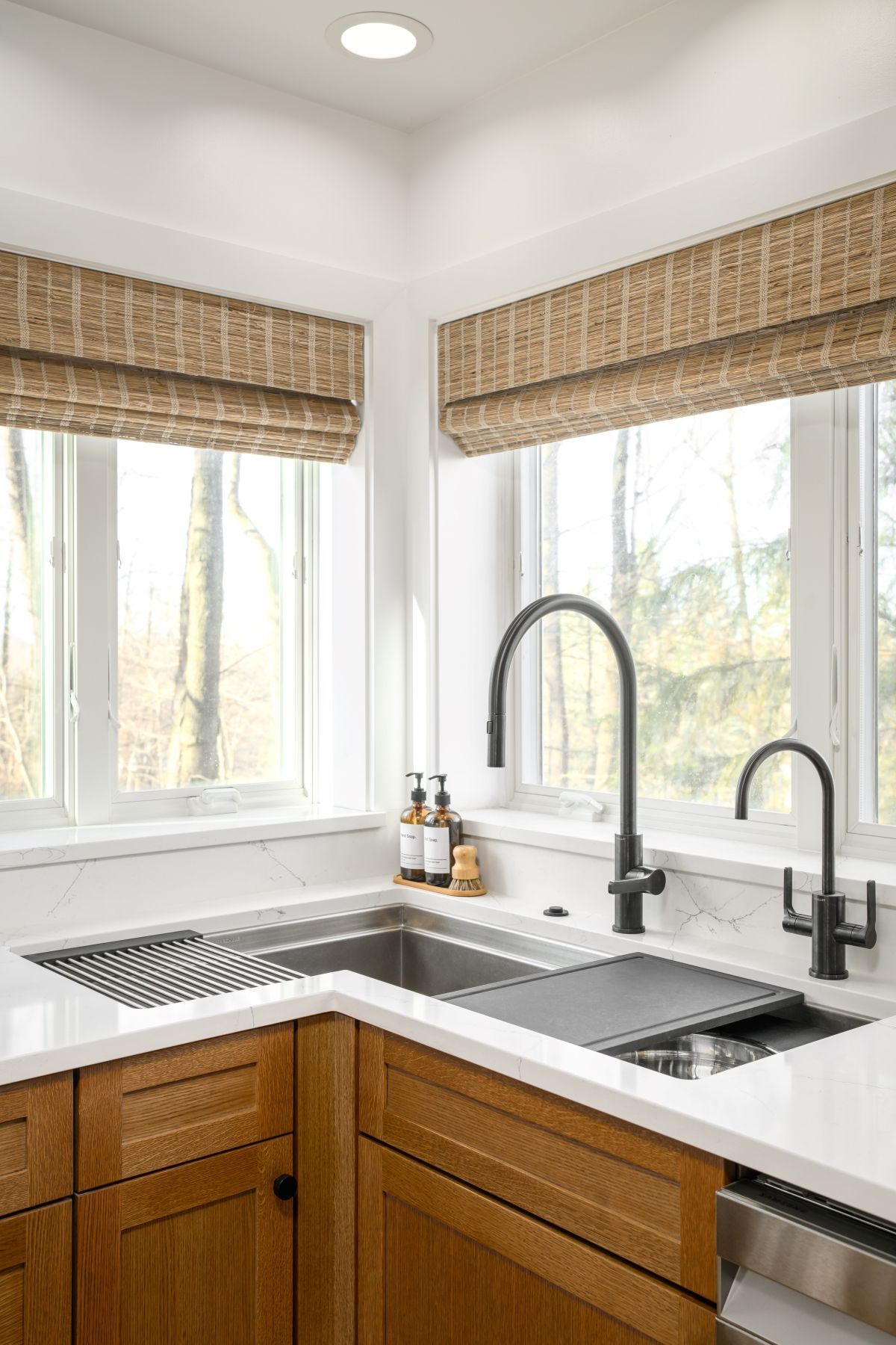 Bright kitchen corner with white cabinets, wood lower drawers, double sink, and woven blinds over windows.