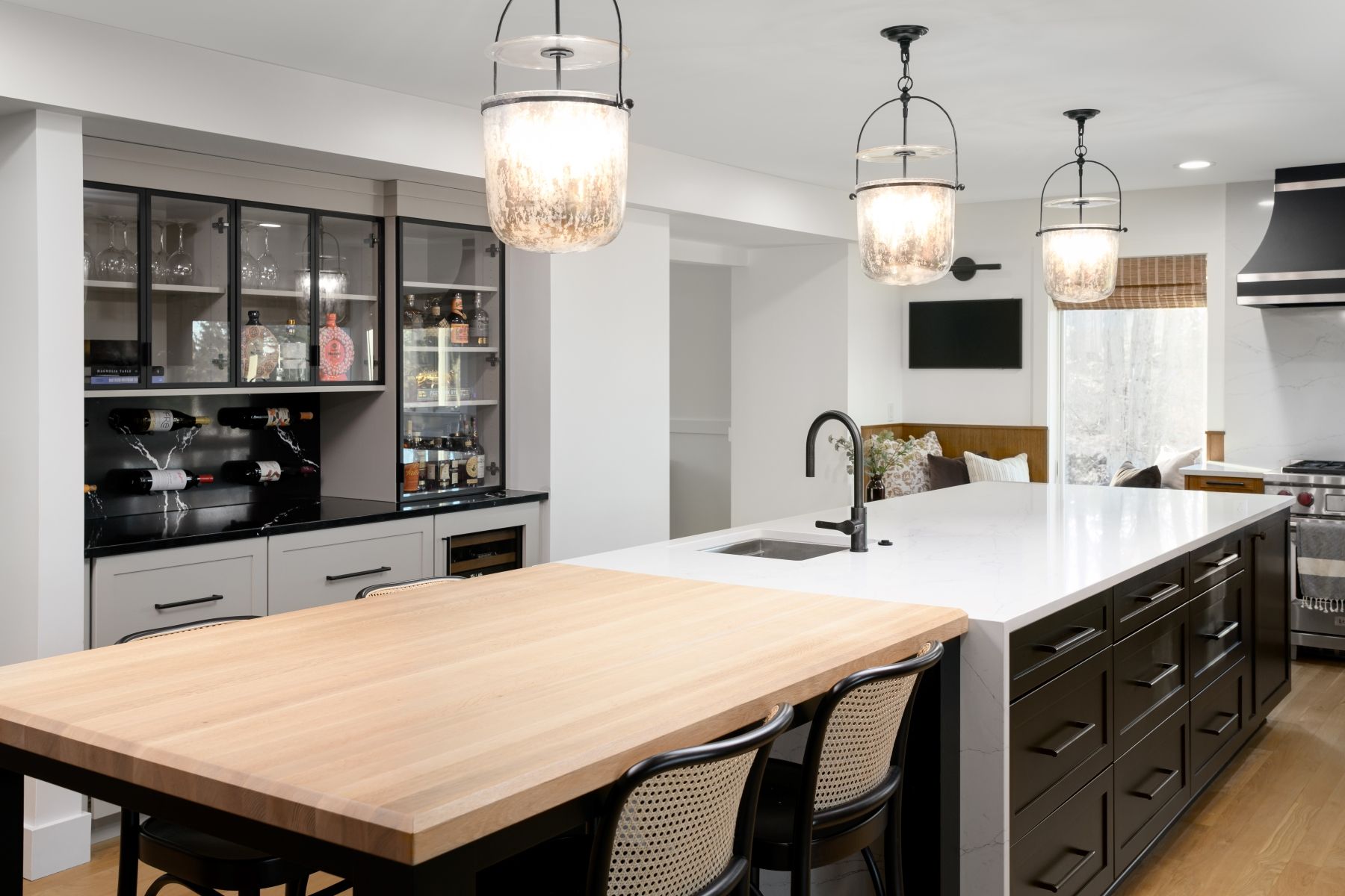 Modern kitchen with large island, pendant lights, wood countertop, dark cabinets, and glass-front display cabinets