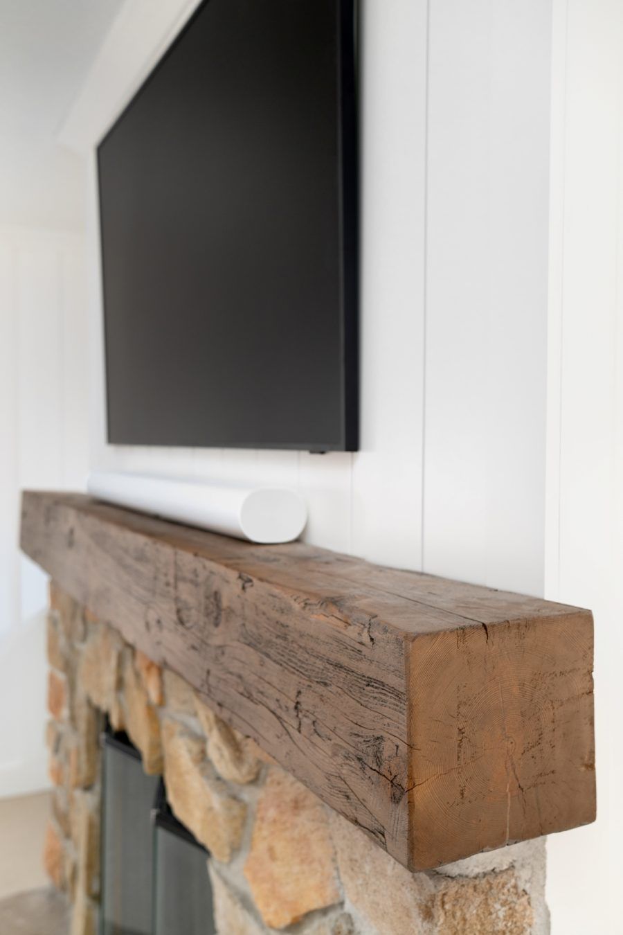 Wall-mounted TV above a rustic wooden mantel on a white wall