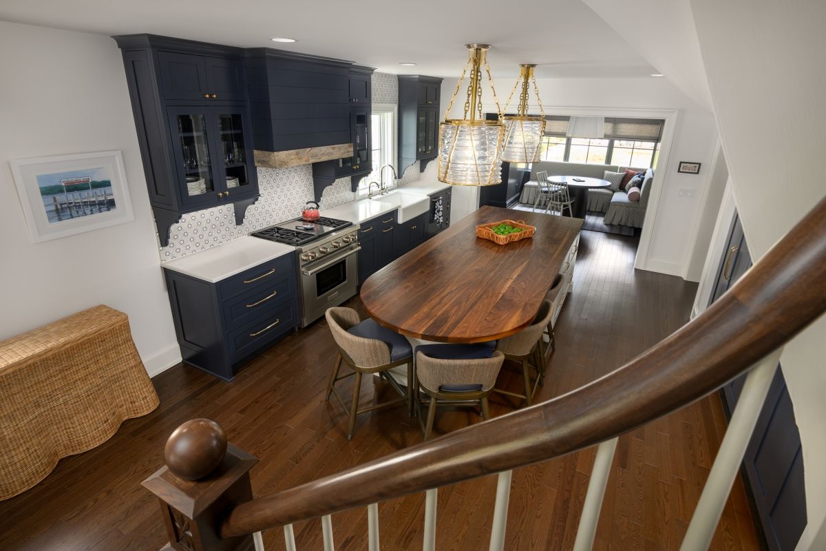 Modern kitchen and dining area with dark cabinets, wooden table, and staircase railing in foreground