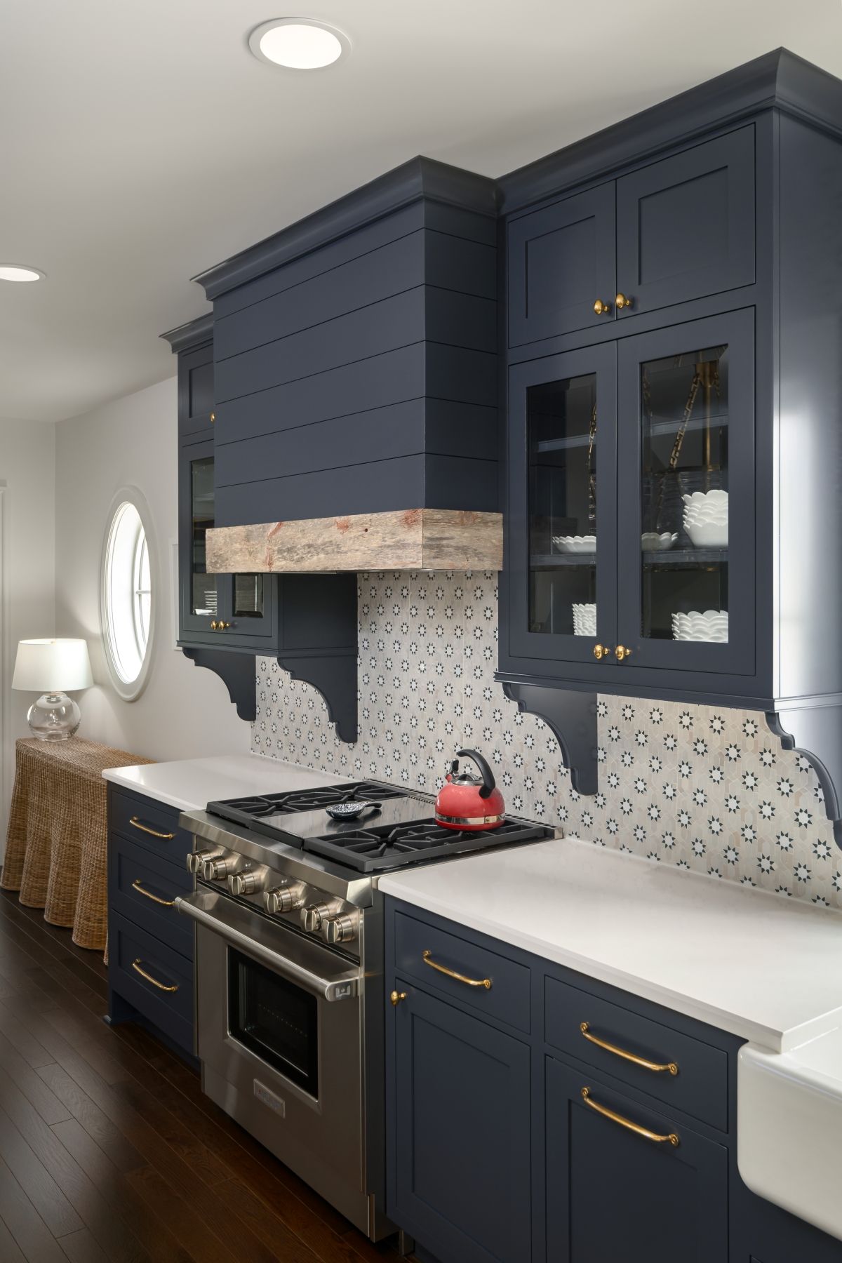 Modern kitchen with navy cabinets, stainless stove, white counters, and patterned backsplash