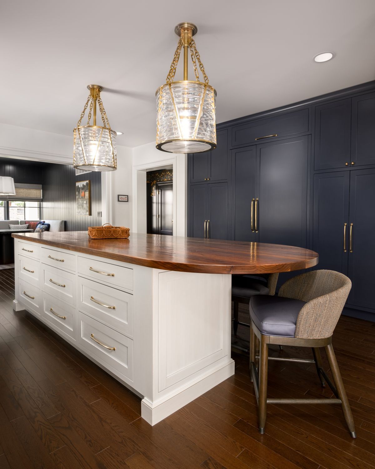 Modern kitchen with white island, dark blue cabinets, wood countertop, and gold pendant lights