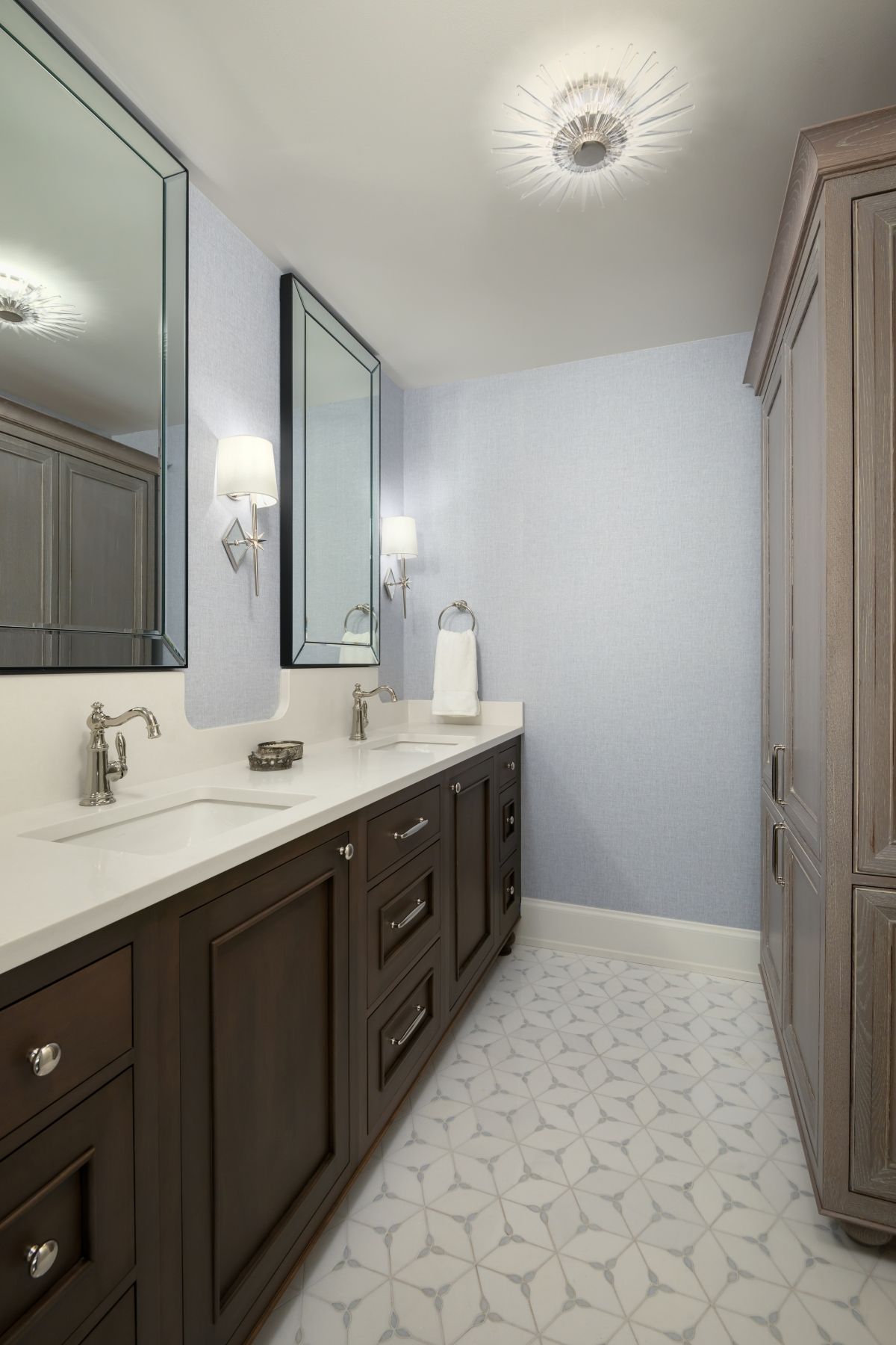 Bright bathroom with dark wood vanity, large mirrors, patterned tile floor, and light blue walls.