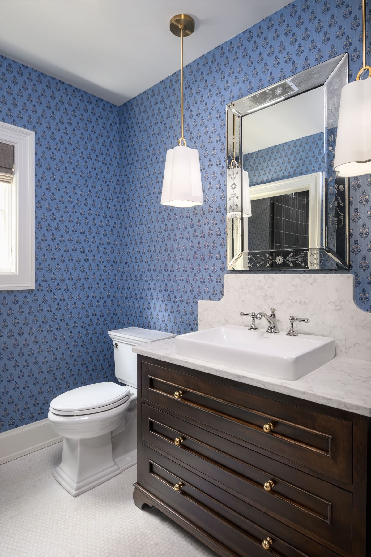 Blue wallpapered bathroom with dark vanity, white sink, toilet, and hanging pendant light