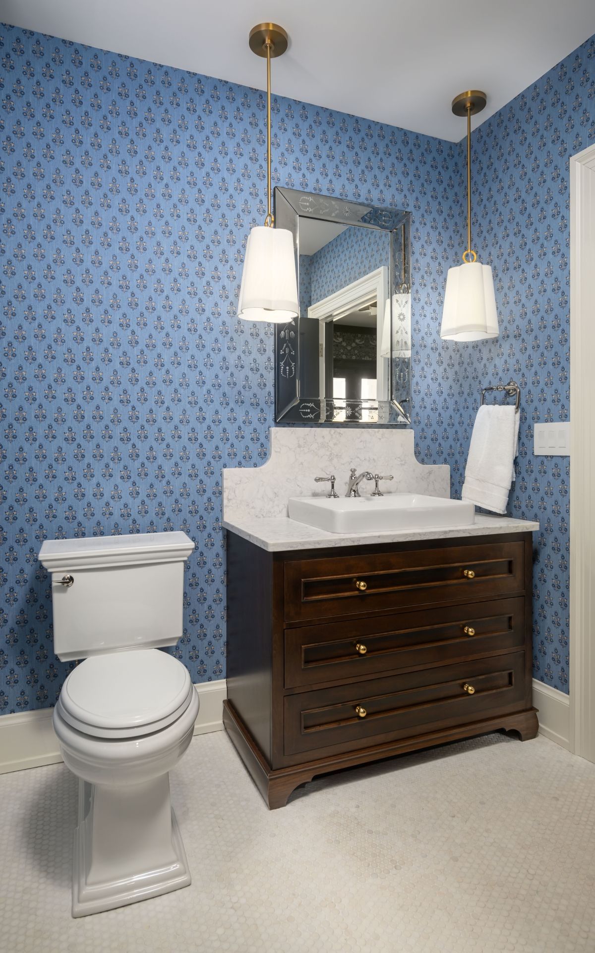 Blue wallpaper bathroom with white toilet, dark wood vanity, mirror, and pendant lights