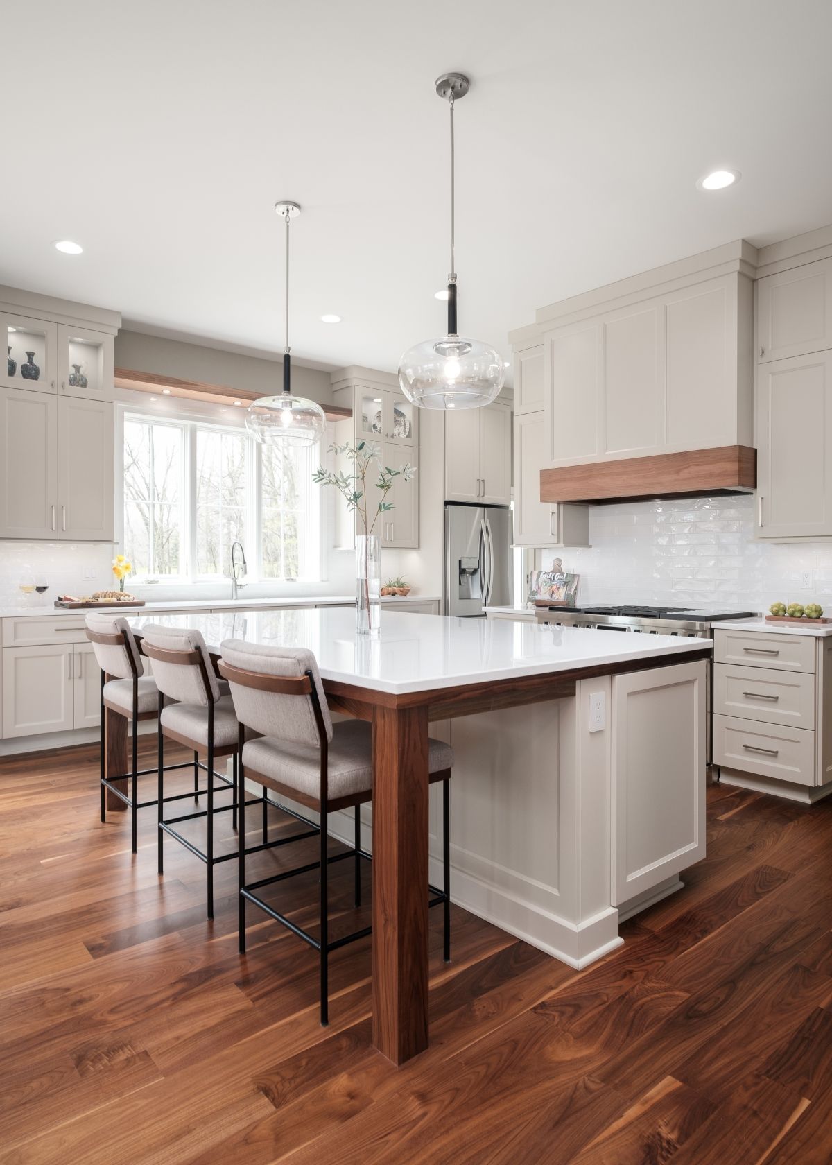 Bright kitchen with white cabinets, large island, pendant lights, and hardwood floors.