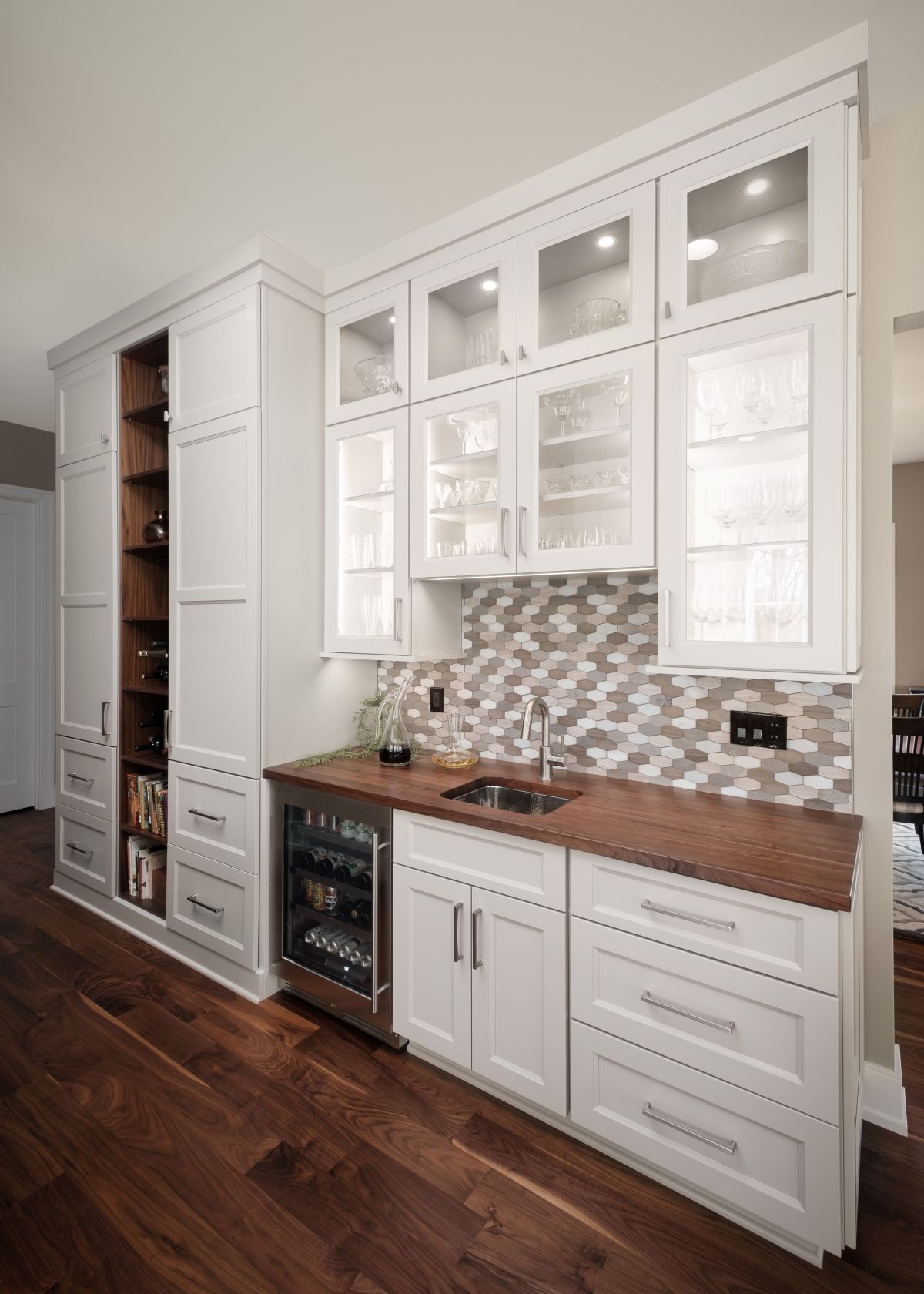 White built-in kitchen cabinet wall with glass fronts, wood countertop, sink, and wine fridge on hardwood floor