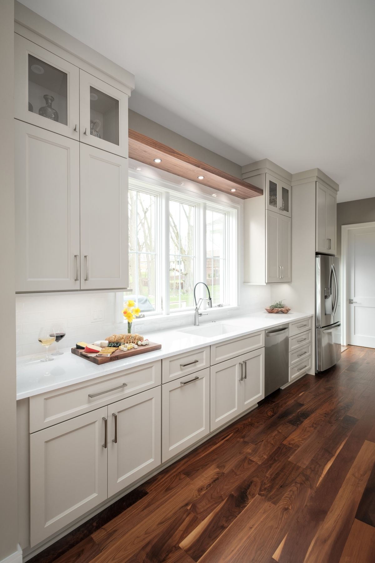 Bright white kitchen with long windows, gray cabinets, and dark hardwood floors