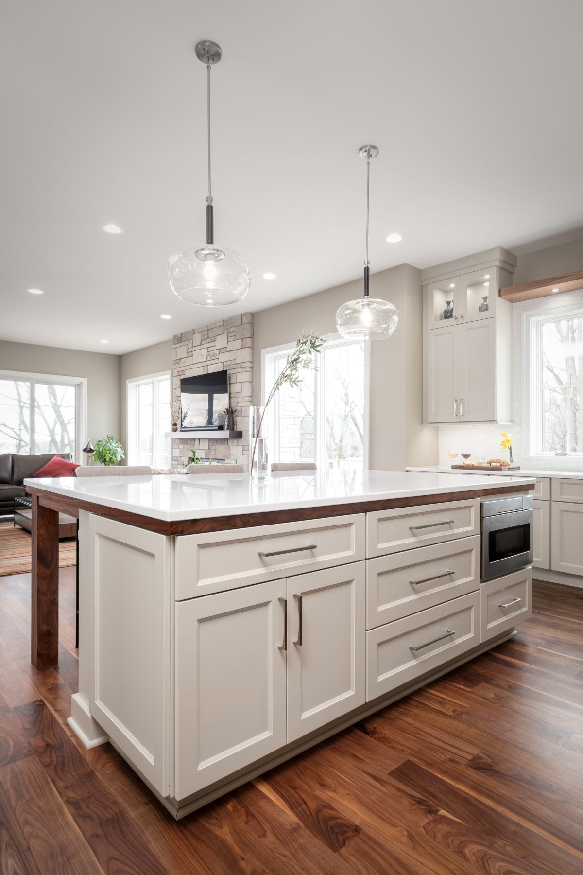 Bright white kitchen with a large island, pendant lights, and wood flooring.
