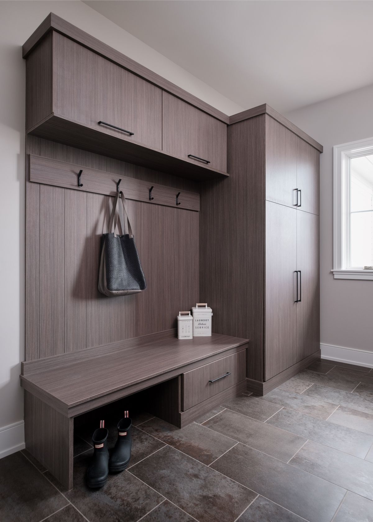 Wood-paneled mudroom bench with hooks, storage cubbies, and tall closet beside a window