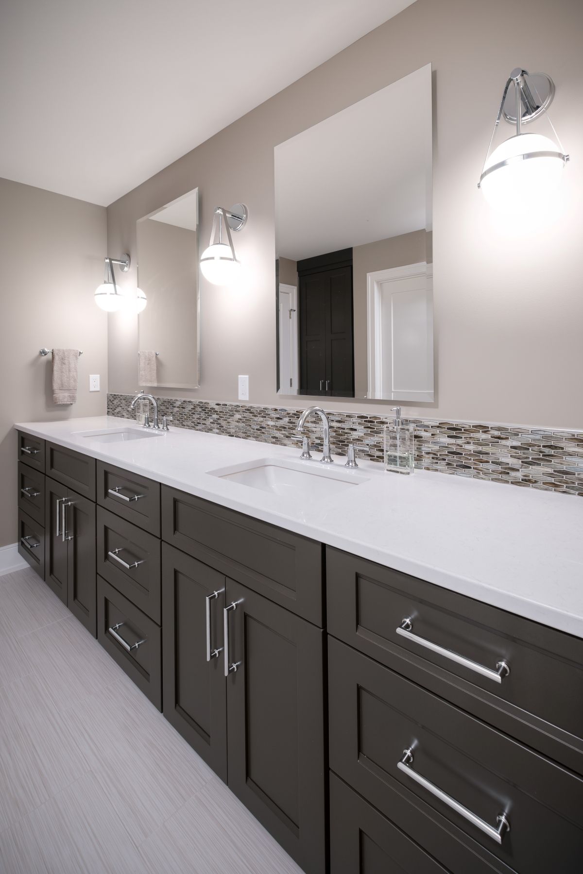 Modern bathroom vanity with dark cabinets, white countertop, large mirrors, and wall sconces