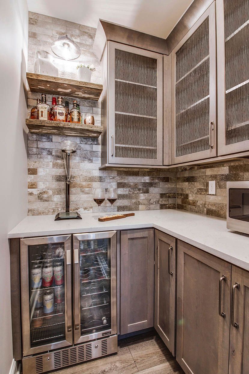 Compact corner kitchen with white cabinets, stone backsplash, wine fridge, and open shelves with bottles
