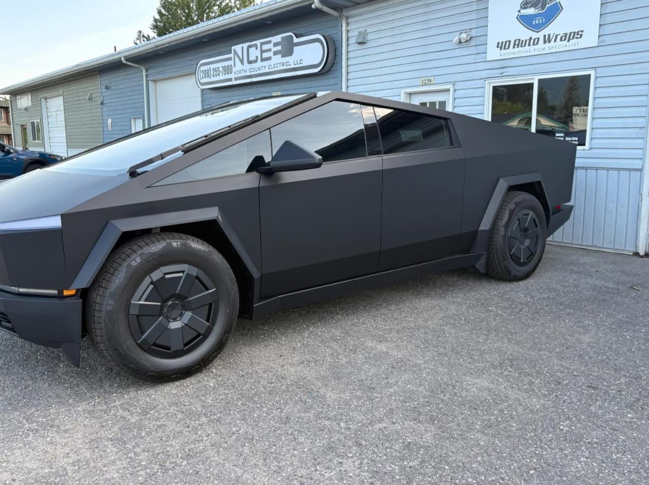 Black Tesla Cybertruck parked outside a building with a sign.