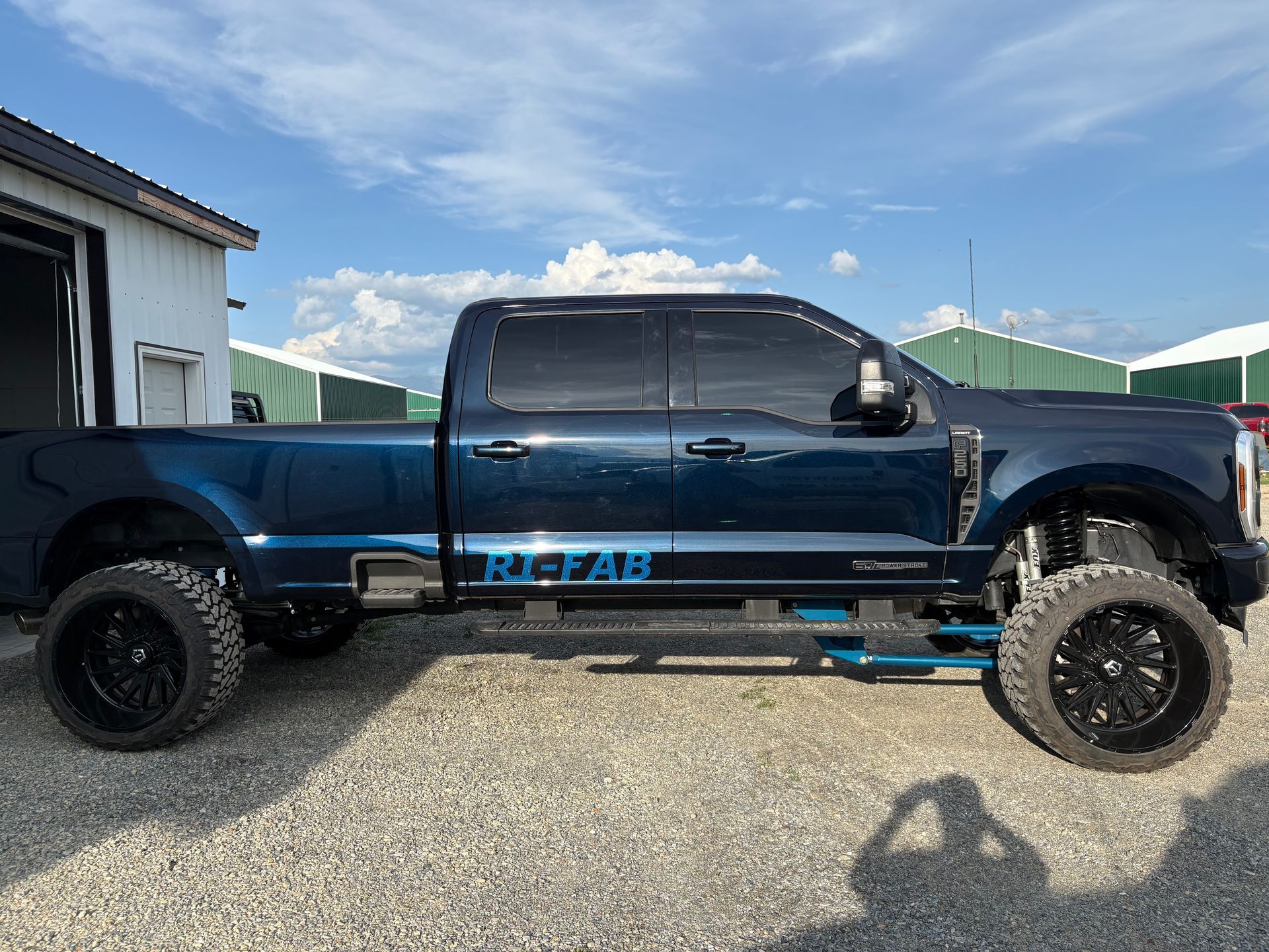 Blue lifted pickup truck with black wheels parked outside on a sunny day.