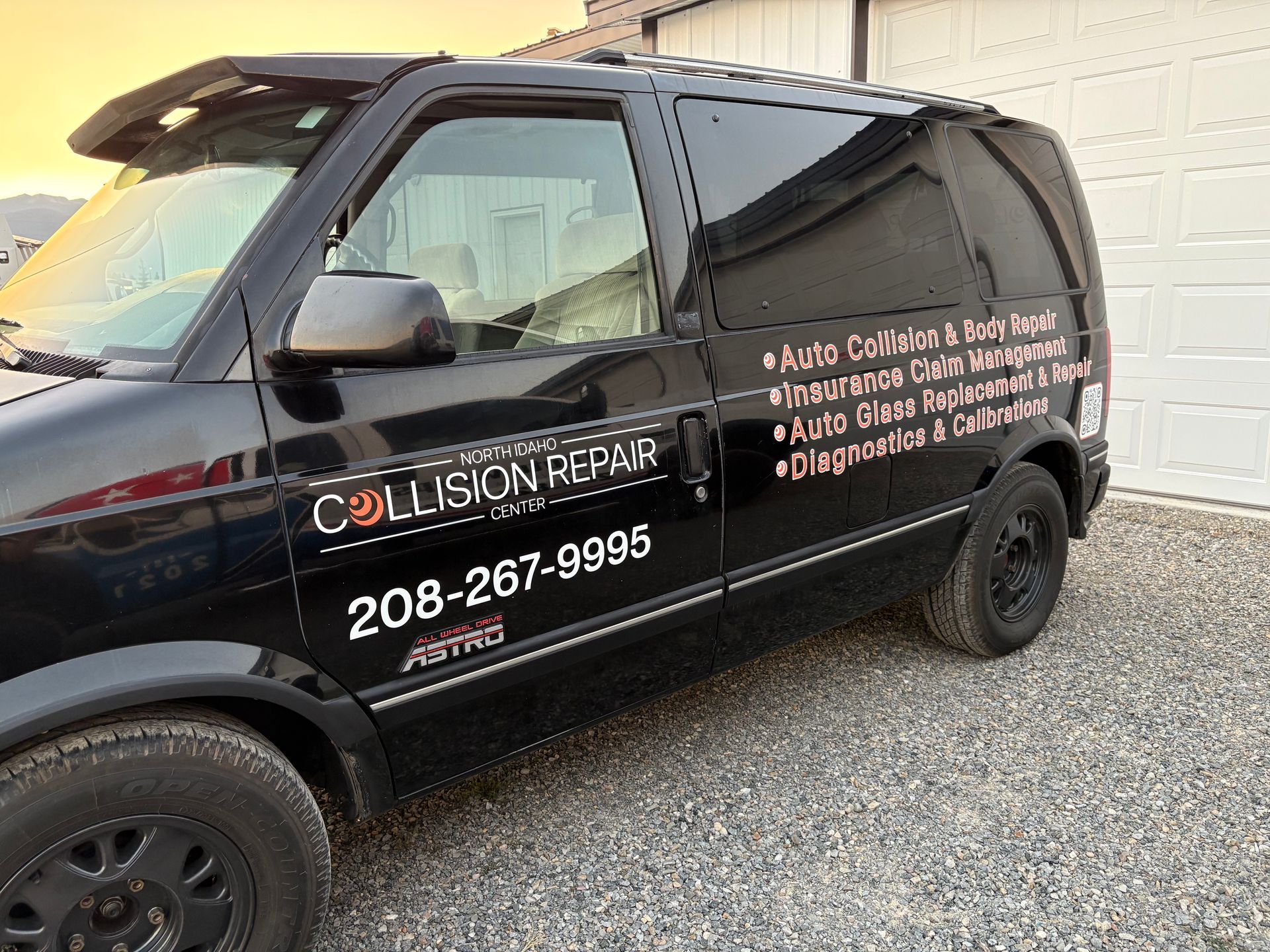 Black Astro van for collision repair, phone number 208-287-9995 on side of a building.