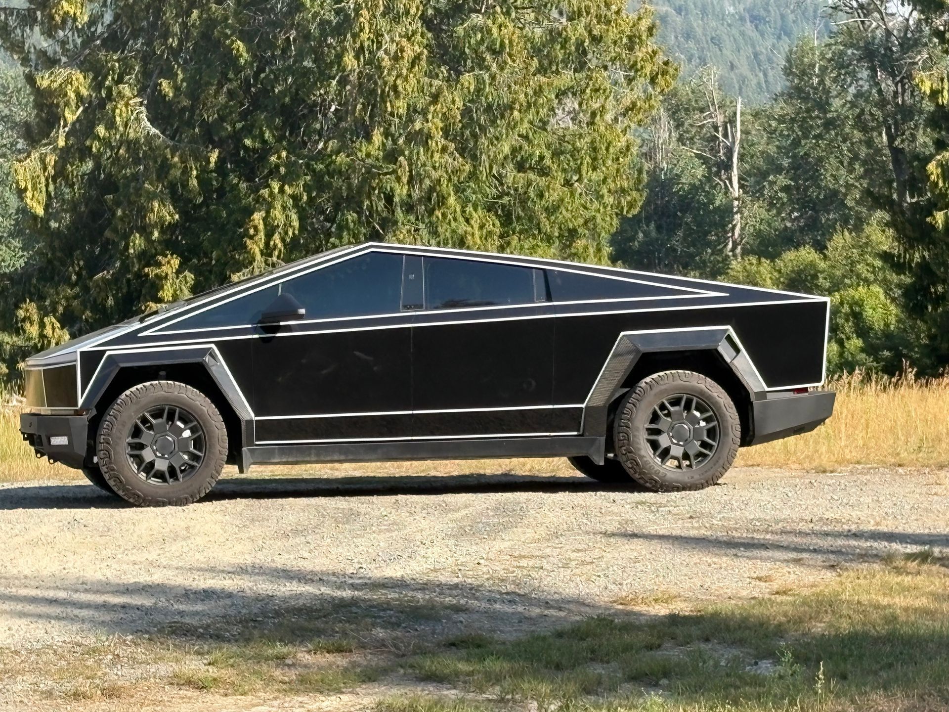 Black Tesla Cybertruck parked on a dirt road with trees in the background.