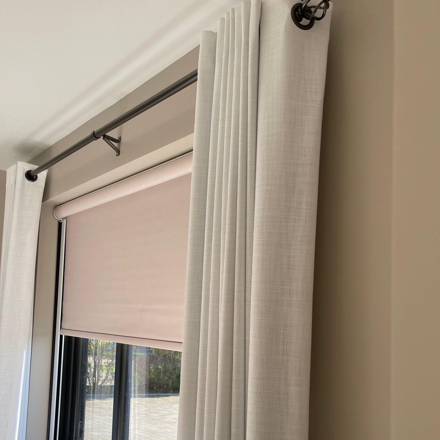 A window with a roman blind on it and a car in the background.