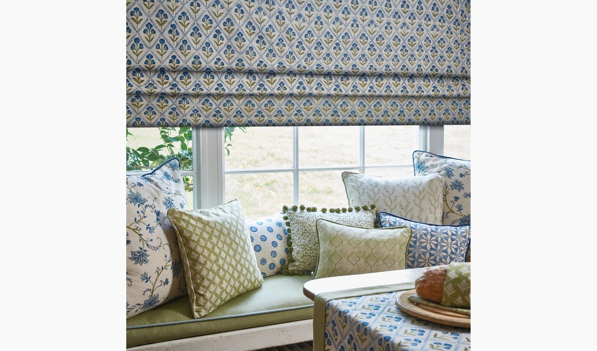 A window seat with lots of pillows and a roman shade