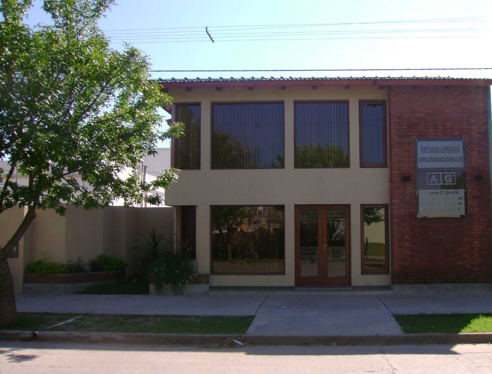 Edificio de oficinas de dos plantas con grandes ventanales, fachada de ladrillo y un árbol delante.