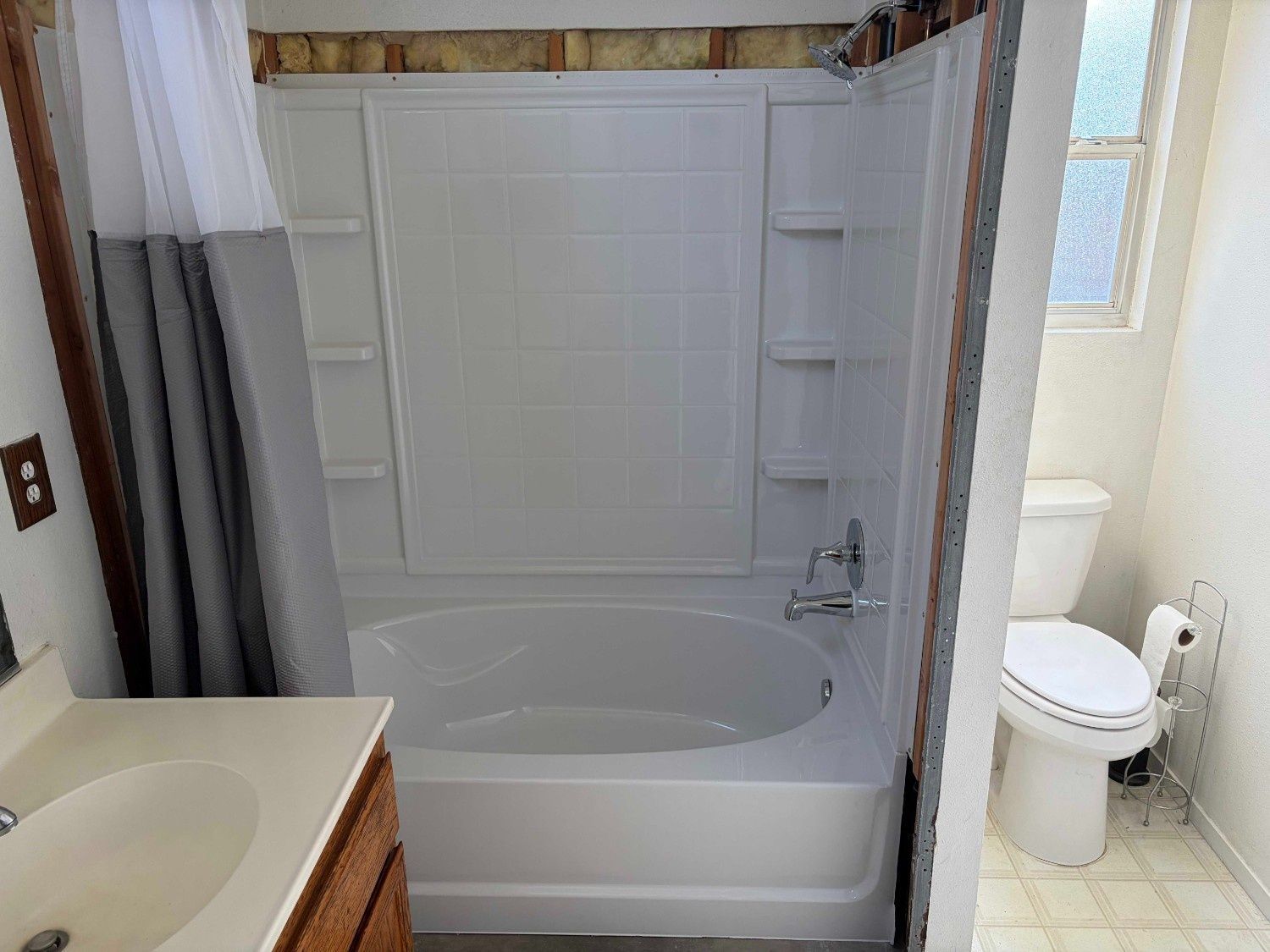 A small bathroom featuring a white tub-shower unit, an adjacent toilet, and a vanity with a light-colored countertop.