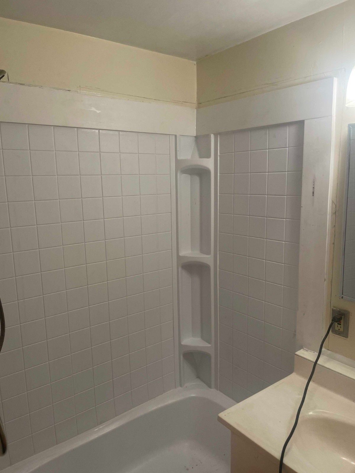 A white bathtub with a white tiled shower surround featuring an integrated shelving unit on the right side.