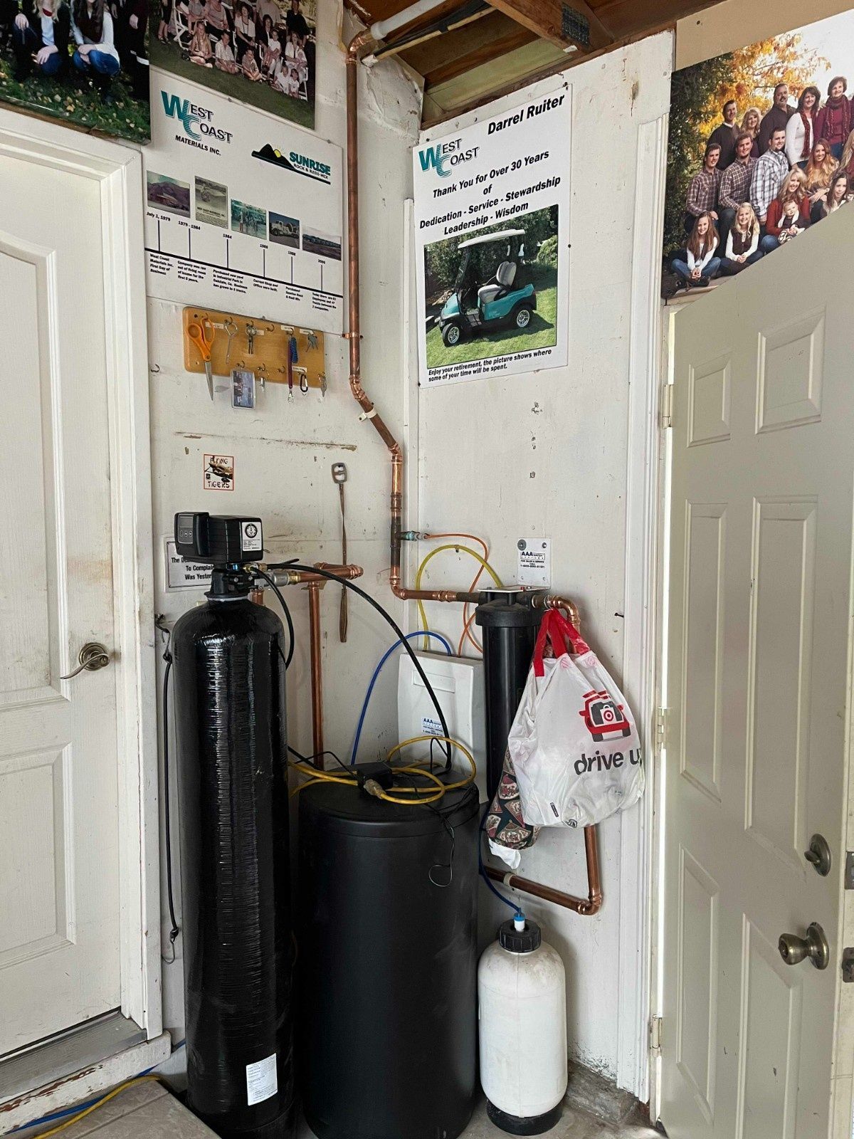A water filtration system with tanks, pipes, and a brine barrel installed against a wall in a garage.