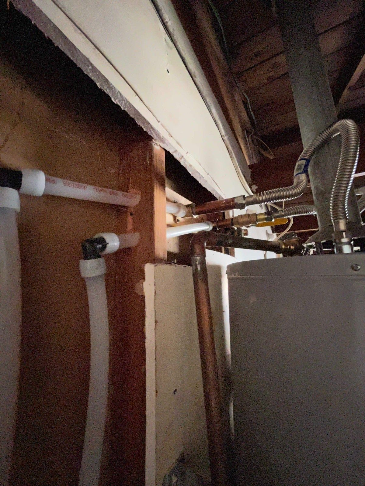Water heater plumbing connections showing white PEX tubing and copper pipes running along wooden wall studs.