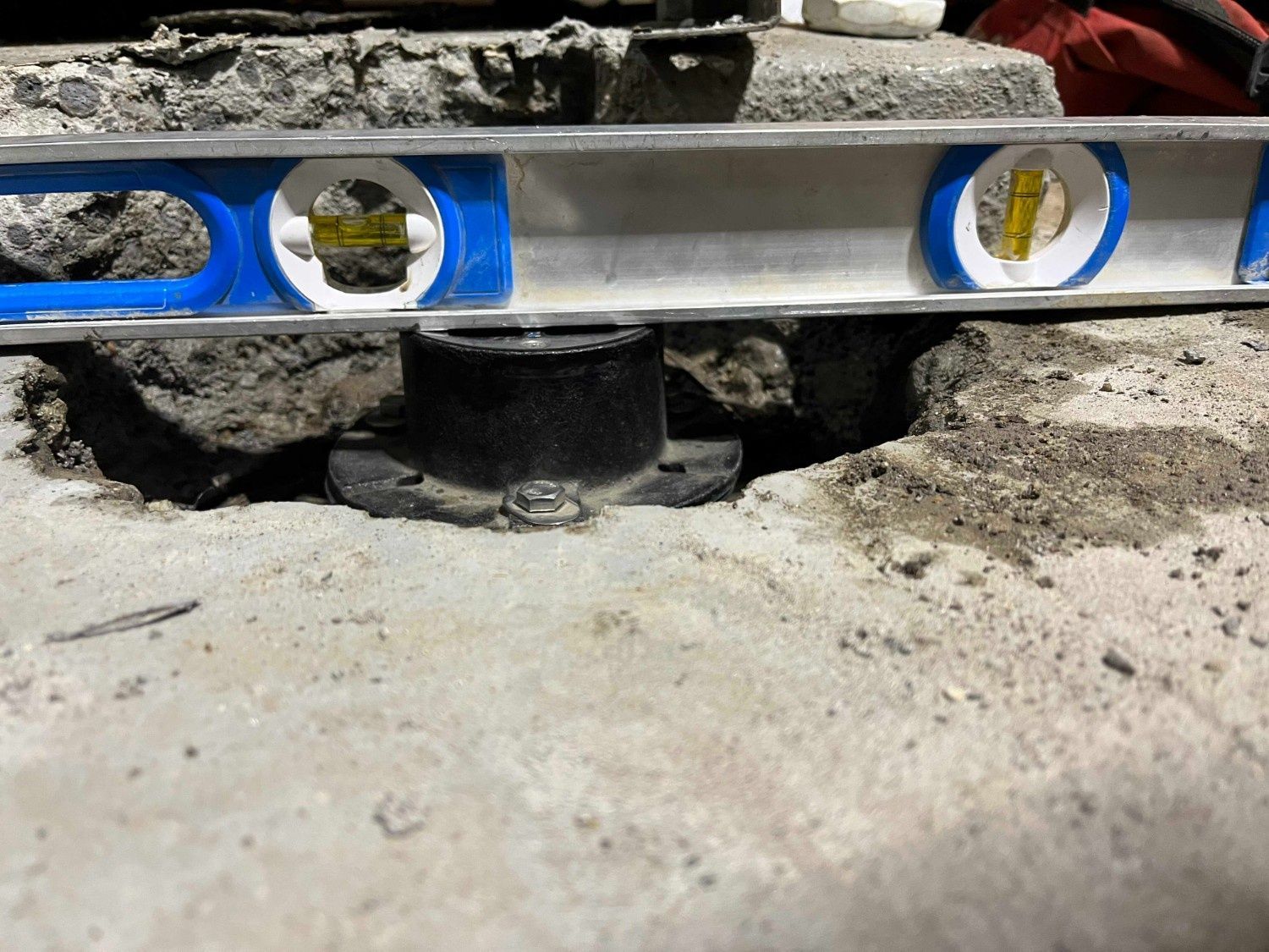 A spirit level placed on a black toilet flange set into a concrete floor, showing it is not level.