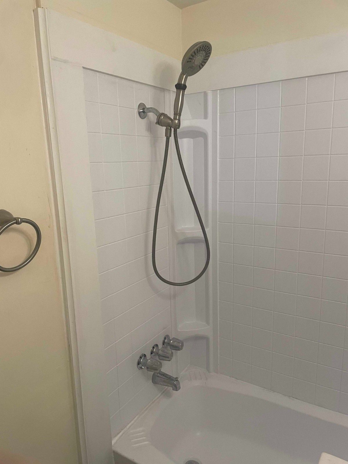 A white shower and bathtub unit featuring a handheld showerhead mounted on a wall bracket with a metal hose.