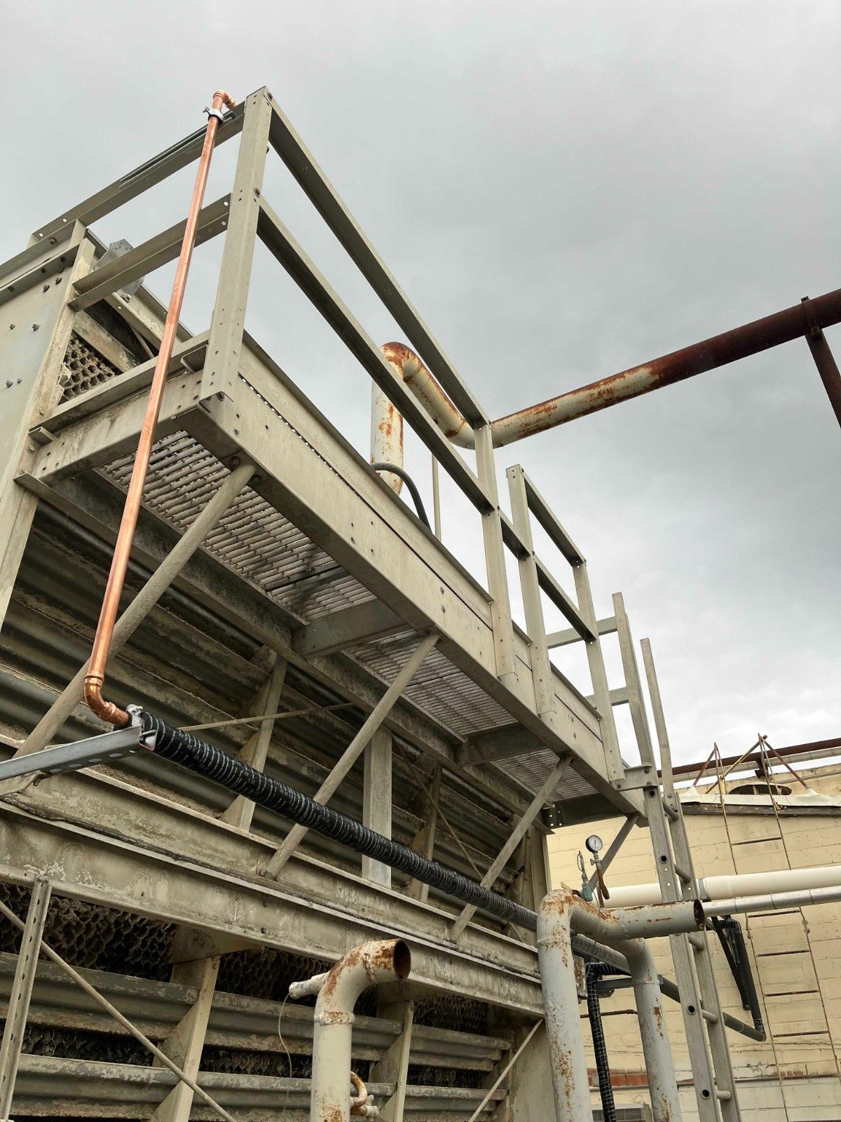 A metal industrial cooling tower structure with pipes and a grated walkway set against a cloudy sky.