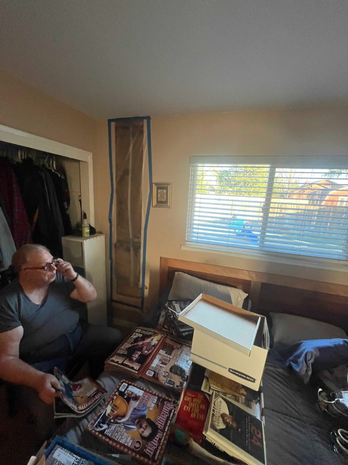 A person sits on a bed in a room, looking at magazines, with a tall, rectangular section of the wall highlighted in blue.