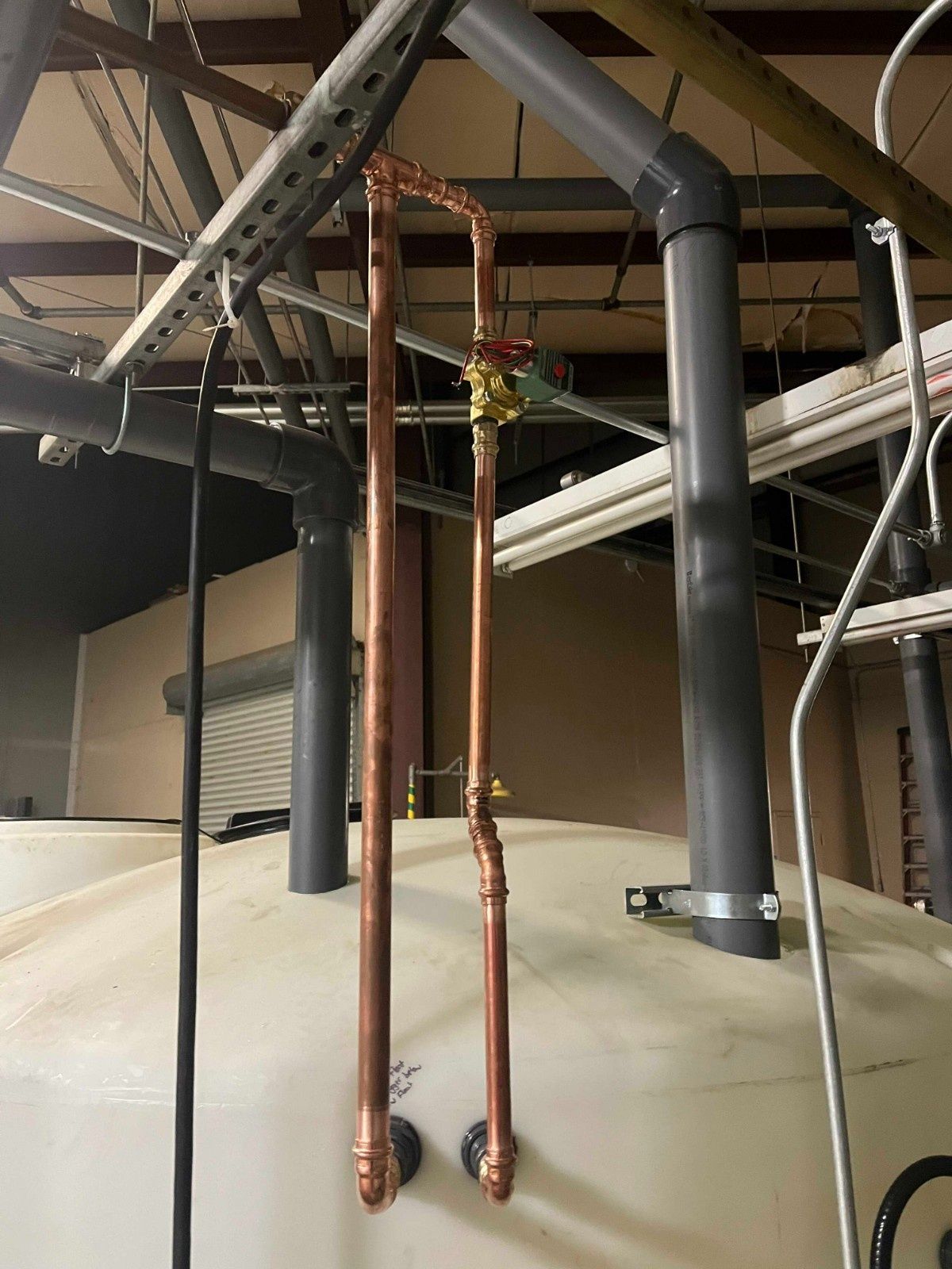 Two copper pipes with a valve connected to the top of a large, white industrial storage tank.