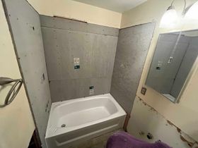 A bathroom renovation in progress, featuring a newly installed white bathtub surrounded by gray cement board wall panels.