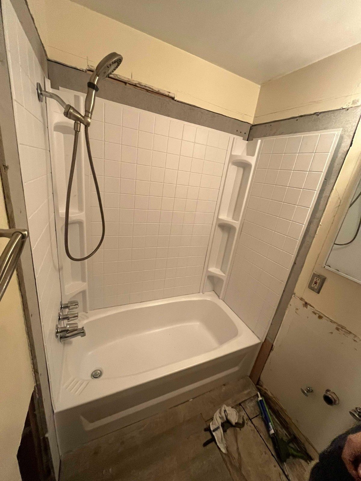 A white shower-tub surround with a handheld shower head, installed in a bathroom under construction with exposed walls.