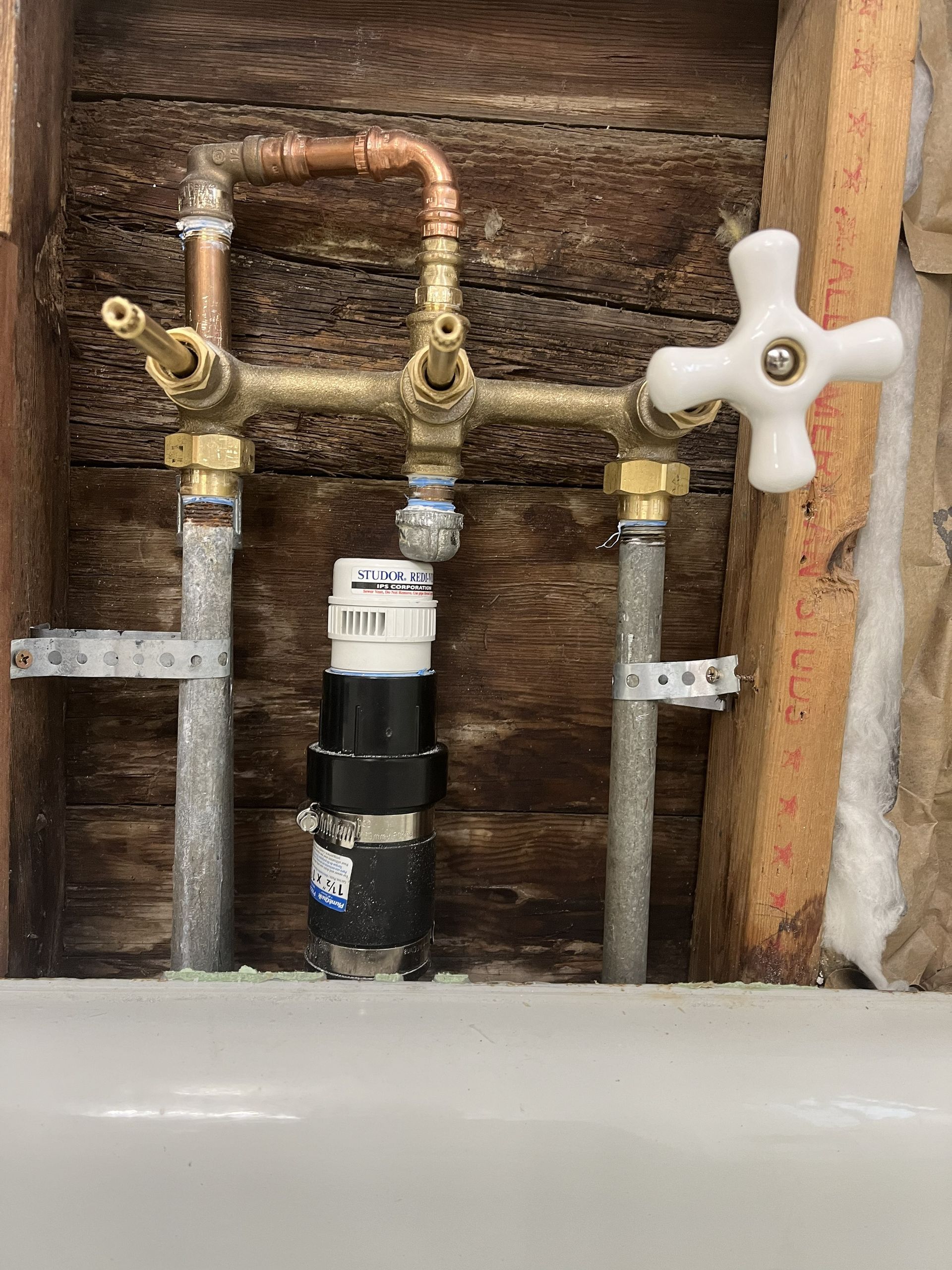 Exposed shower plumbing setup with brass valves, copper piping, and a central white pipe fitting mounted to wood studs.