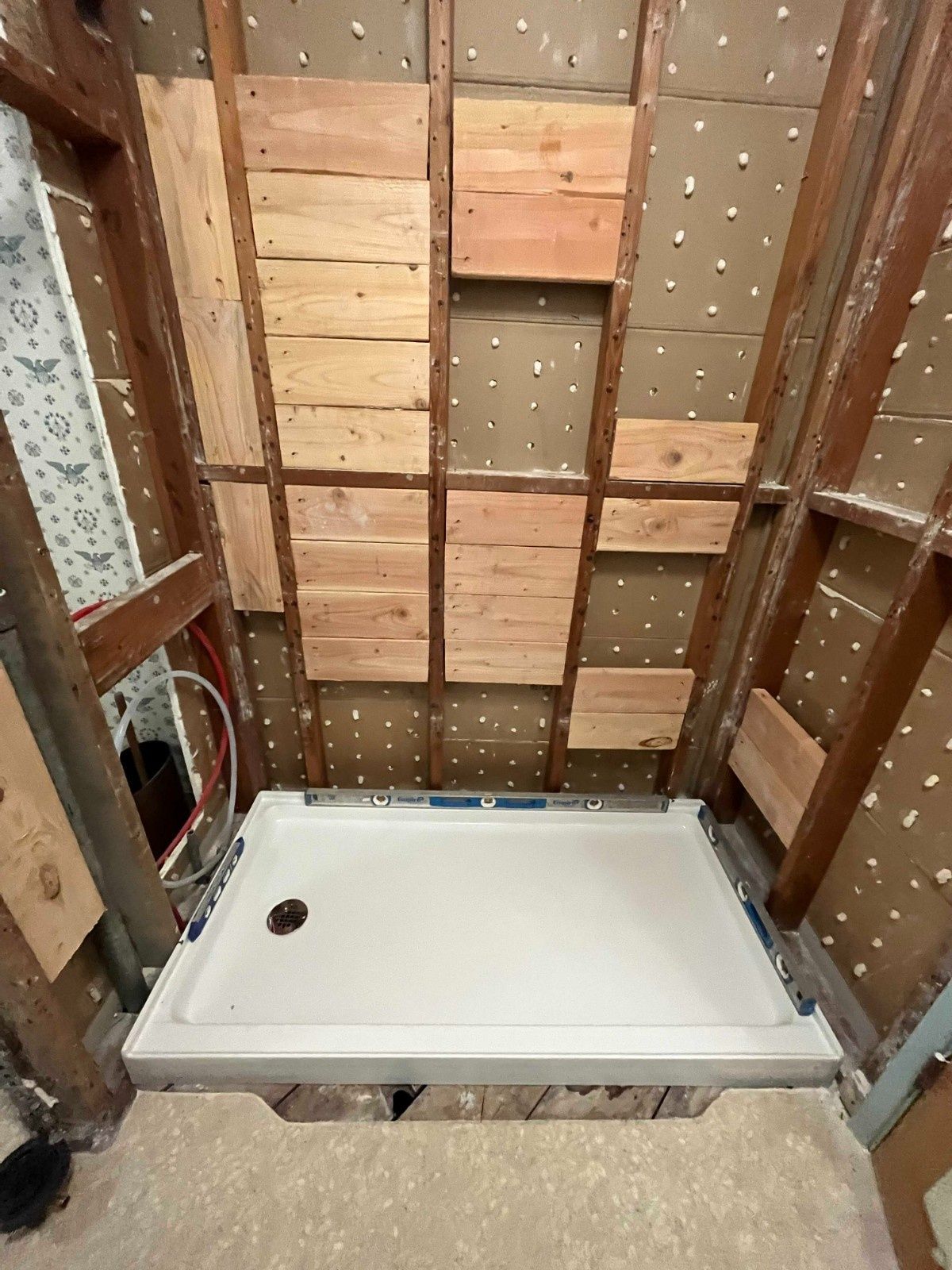 A newly installed white shower base sits in a bathroom frame with exposed wooden studs and backer board walls.