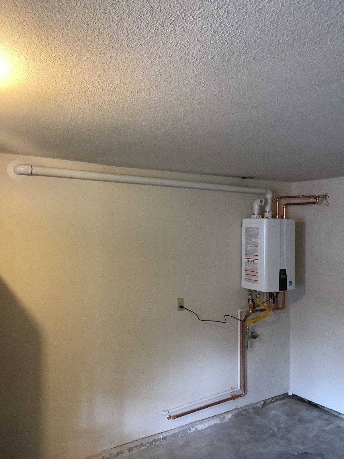 A wall-mounted tankless water heater with connected copper piping and a white vent pipe running horizontally along the wall.