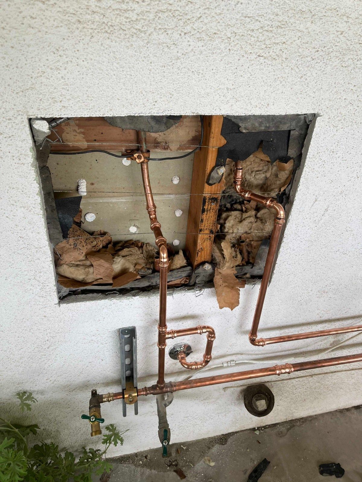 Exposed copper plumbing pipes mounted on an exterior wall with a square section cut into the stucco finish.