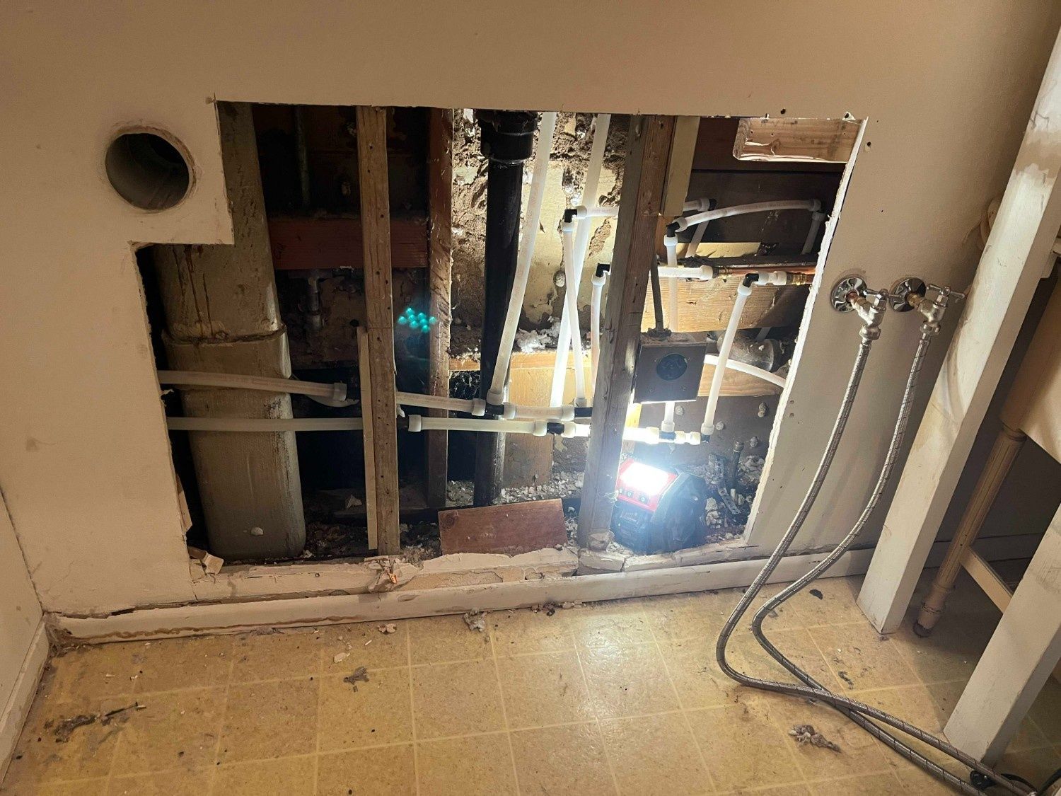 A wall cutout reveals exposed plumbing pipes, wooden studs, and electrical wiring behind a sink area.