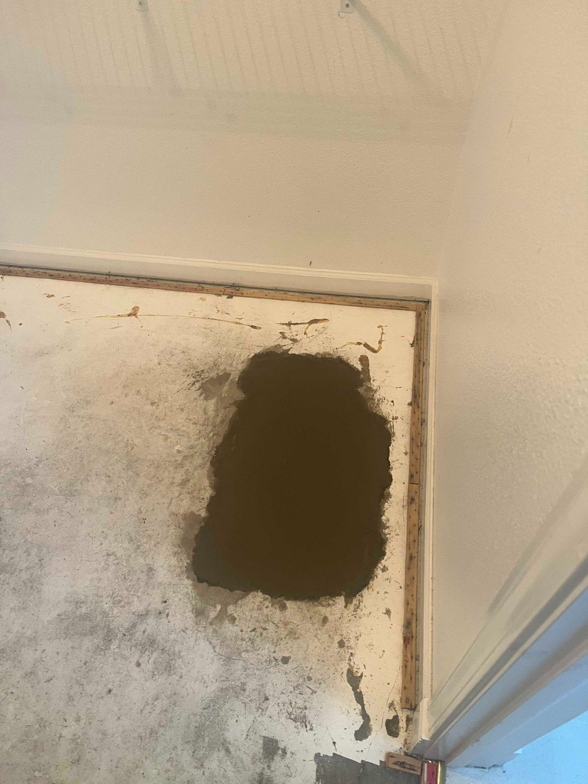 A large dark stain on a beige concrete floor in the corner of a room.