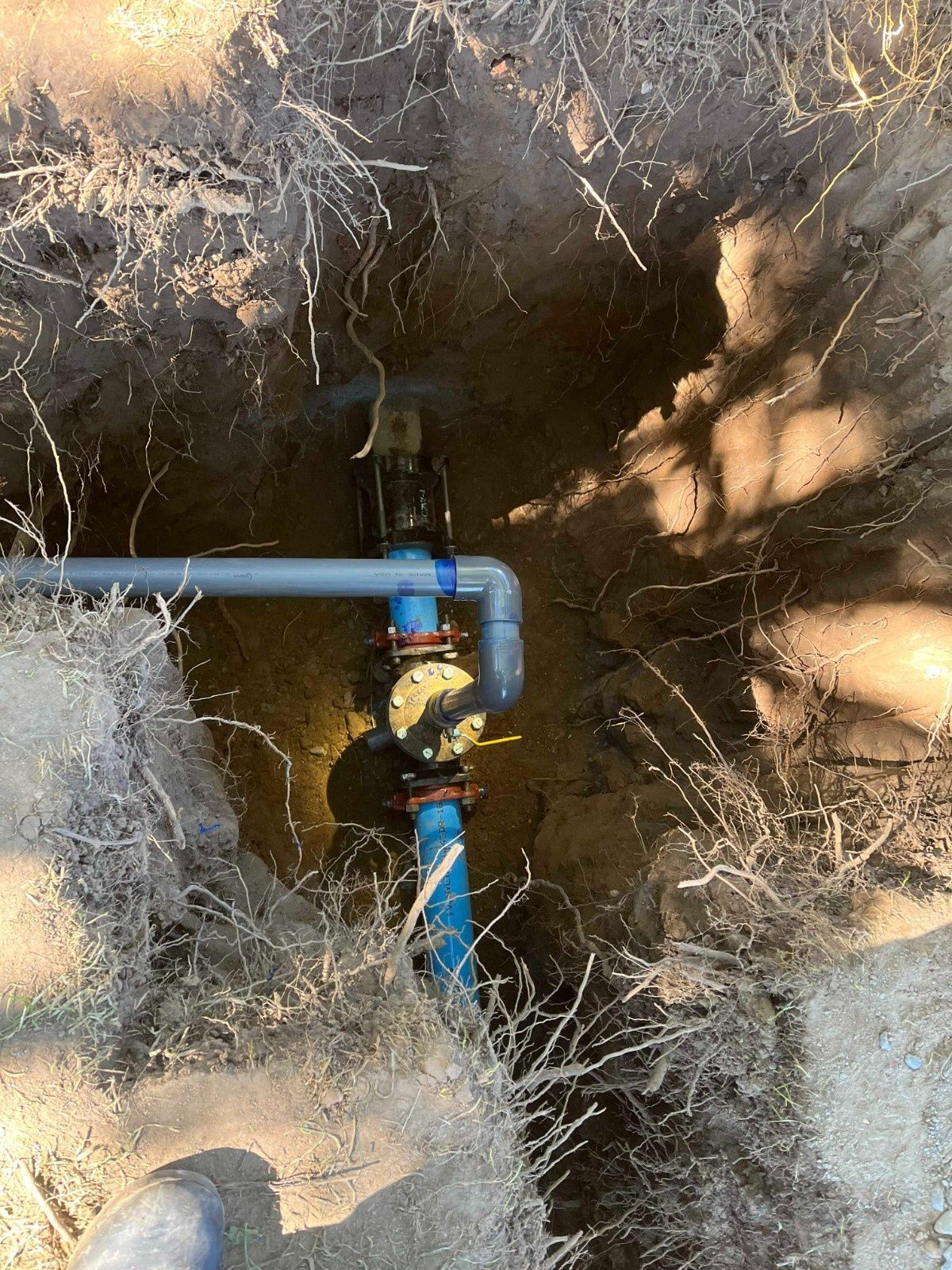 A view from above showing a blue pipe and a circular valve component installed within an excavated dirt trench.